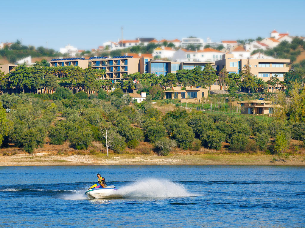 拉戈芒塔格别墅瑙酒店 蒙塔吉尔 外观 照片 The photo depicts a person riding a jet ski on a body of water. In the background, there are modern buildings and lush greenery, suggesting a scenic landscape, likely near a resort or upscale residential area. The clear blue sky and calm water enhanc