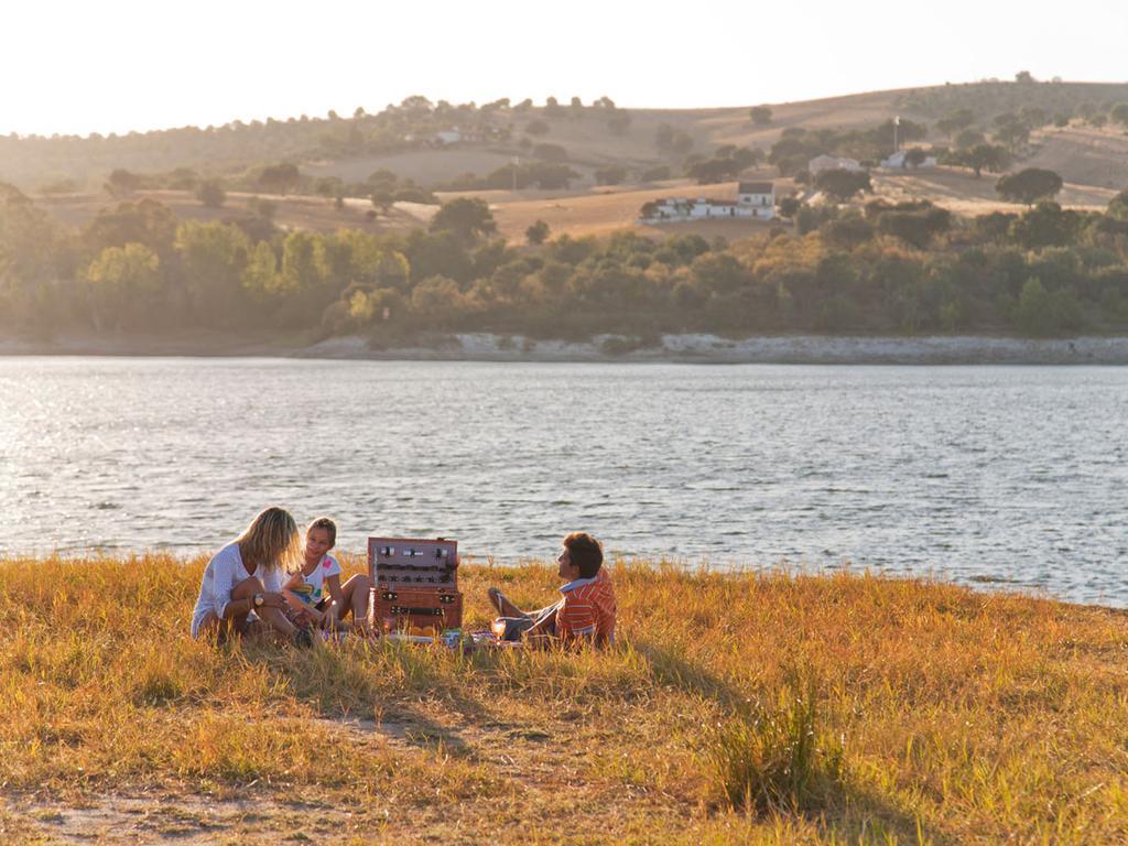 拉戈芒塔格别墅瑙酒店 蒙塔吉尔 外观 照片 The photo depicts a serene lakeside scene during sunset. Three people are gathered on a grassy area near the water, enjoying a picnic. They are seated around a picnic basket, with the shimmering lake in the background and hills in the distance. The w