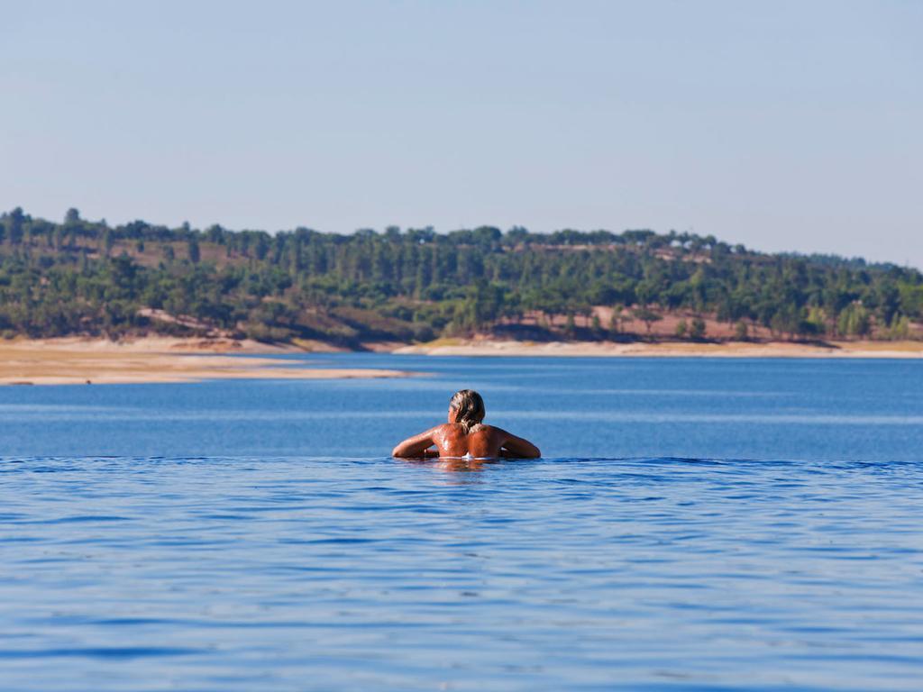 拉戈芒塔格别墅瑙酒店 蒙塔吉尔 外观 照片 The photo shows a person swimming in a calm body of water, likely a lake or a river. The swimmer is seen from behind and appears to be enjoying the water on a sunny day. In the background, there's a scenic landscape featuring green trees and a sandy 