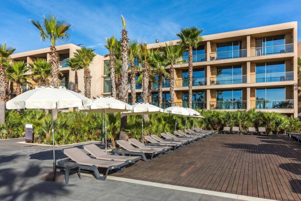 拉戈芒塔格别墅瑙酒店 蒙塔吉尔 外观 照片 The photo shows a modern resort or hotel area featuring several lounge chairs lined up on a wooden deck. Each lounge chair is paired with a white umbrella, providing shade. In the background, there are palm trees, which add to the tropical atmosphere