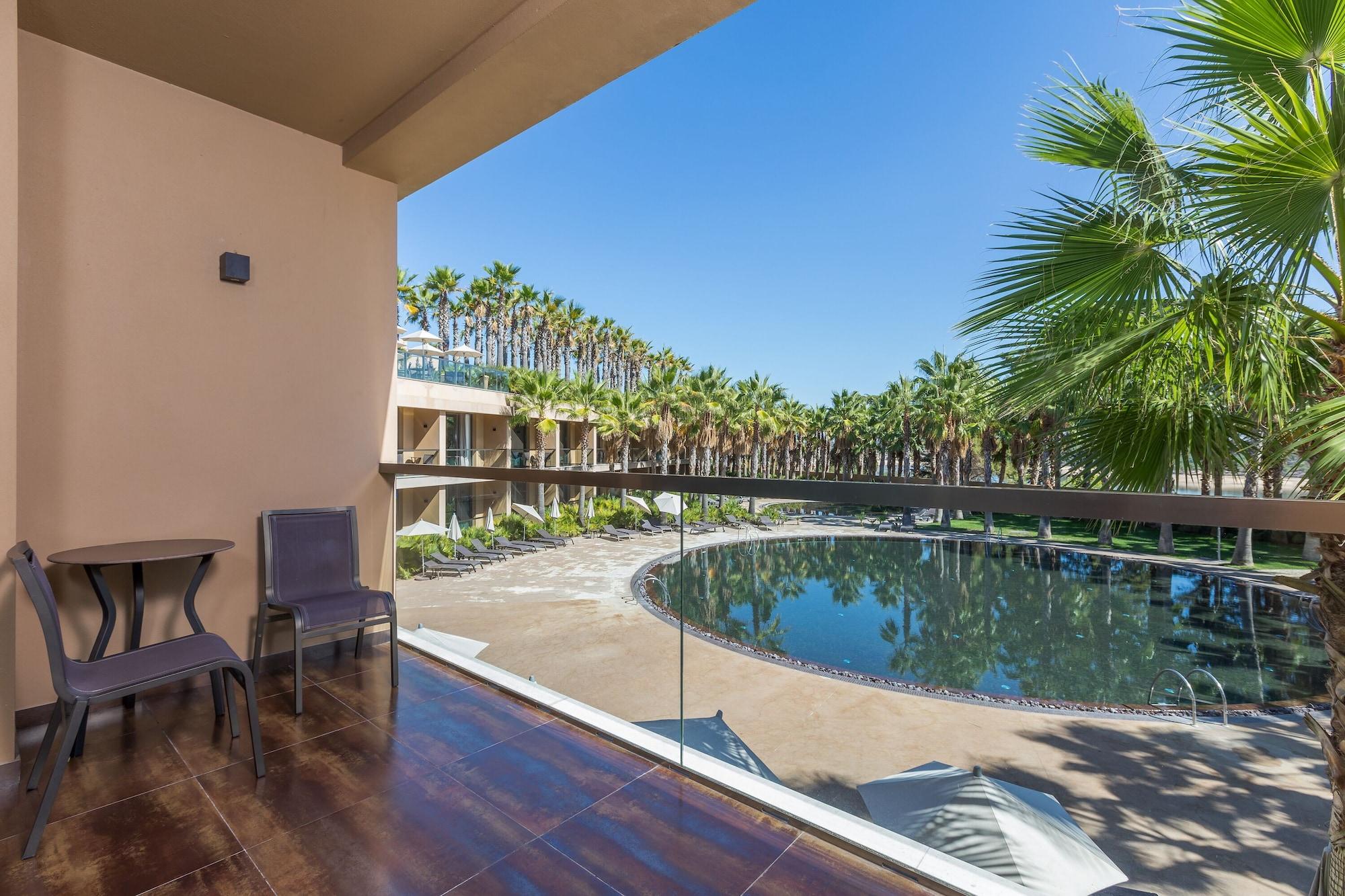 拉戈芒塔格别墅瑙酒店 蒙塔吉尔 外观 照片 The photo shows a balcony view of a resort area. There is a small round table with two chairs on the balcony, providing a spot to sit and enjoy the view. Below, a large, circular pool is visible, surrounded by palm trees and sun loungers. The sky is 