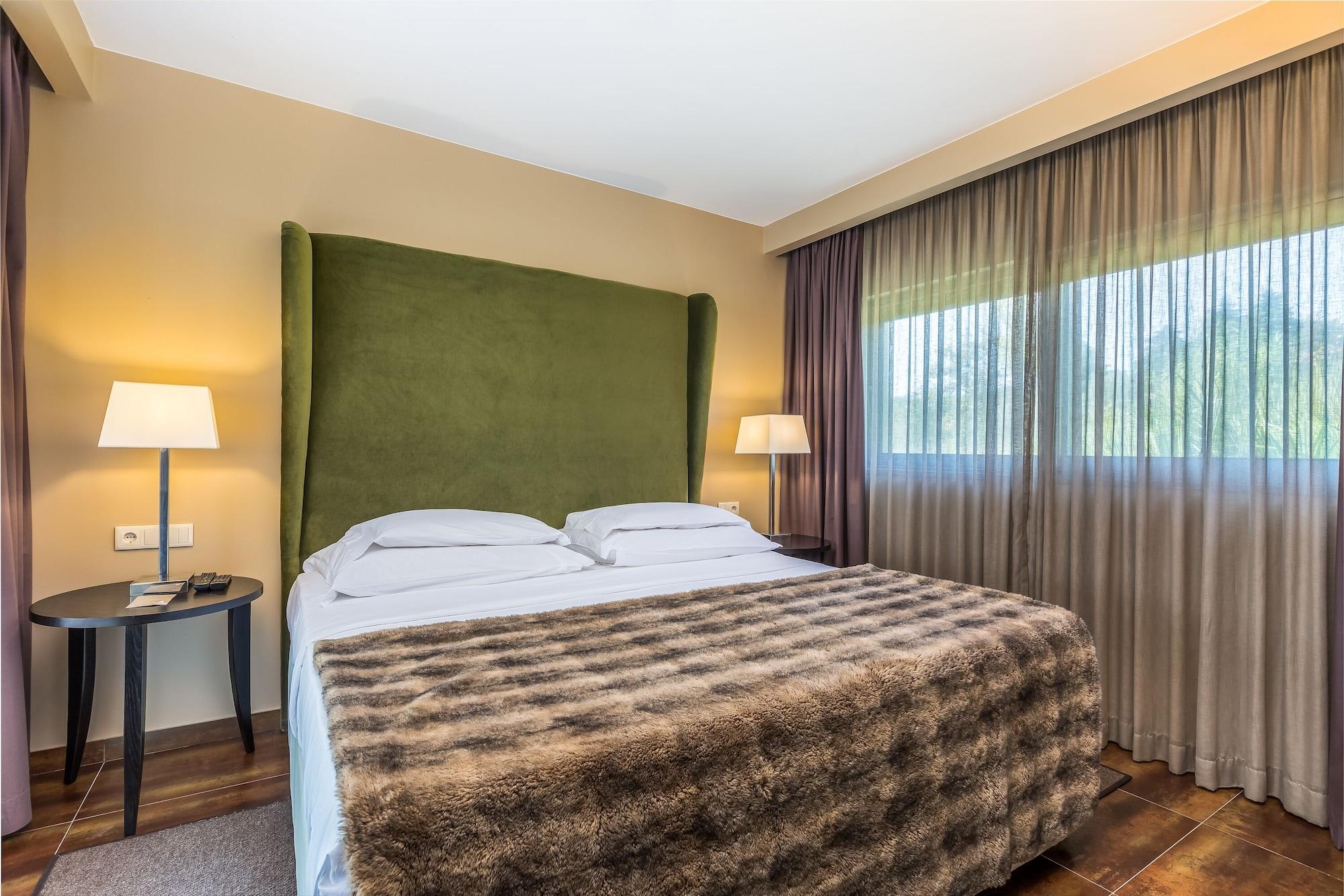 拉戈芒塔格别墅瑙酒店 蒙塔吉尔 外观 照片 The photo shows a cozy hotel room featuring a large bed with two white pillows and a fur-style blanket draped over it. Behind the bed is a tall, green headboard that adds a touch of color to the room. On either side of the bed are bedside tables, eac
