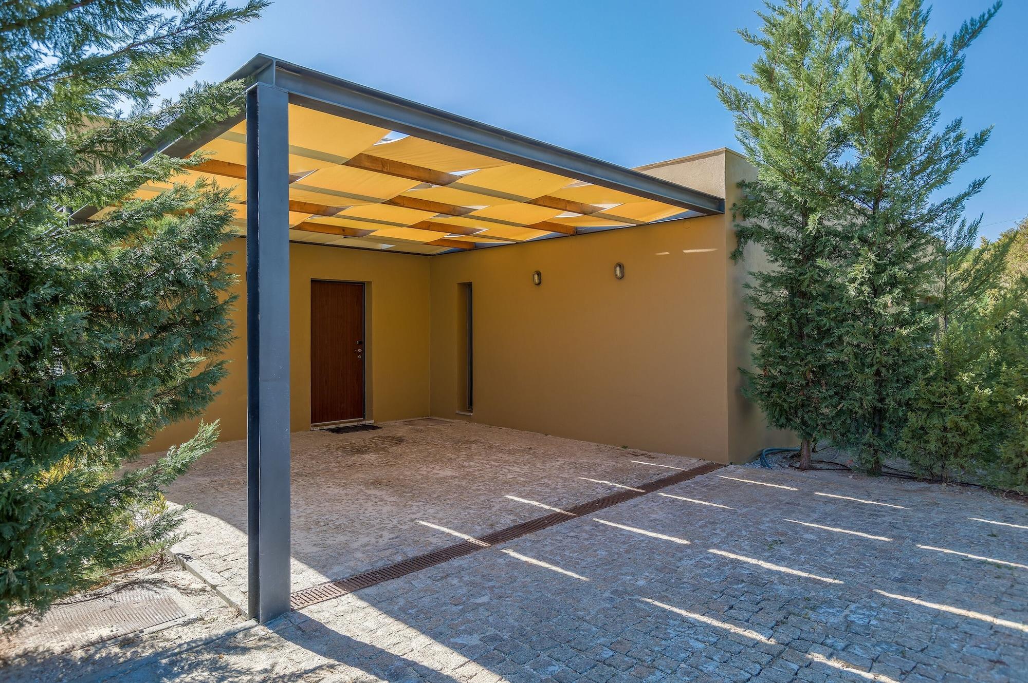拉戈芒塔格别墅瑙酒店 蒙塔吉尔 外观 照片 The photo shows an exterior view of a modern structure with a carport. The carport has a sleek, metallic frame and a yellowish canopy above it. In front of the structure, there is a paved area made of stone or tiles. The main entrance features a wood