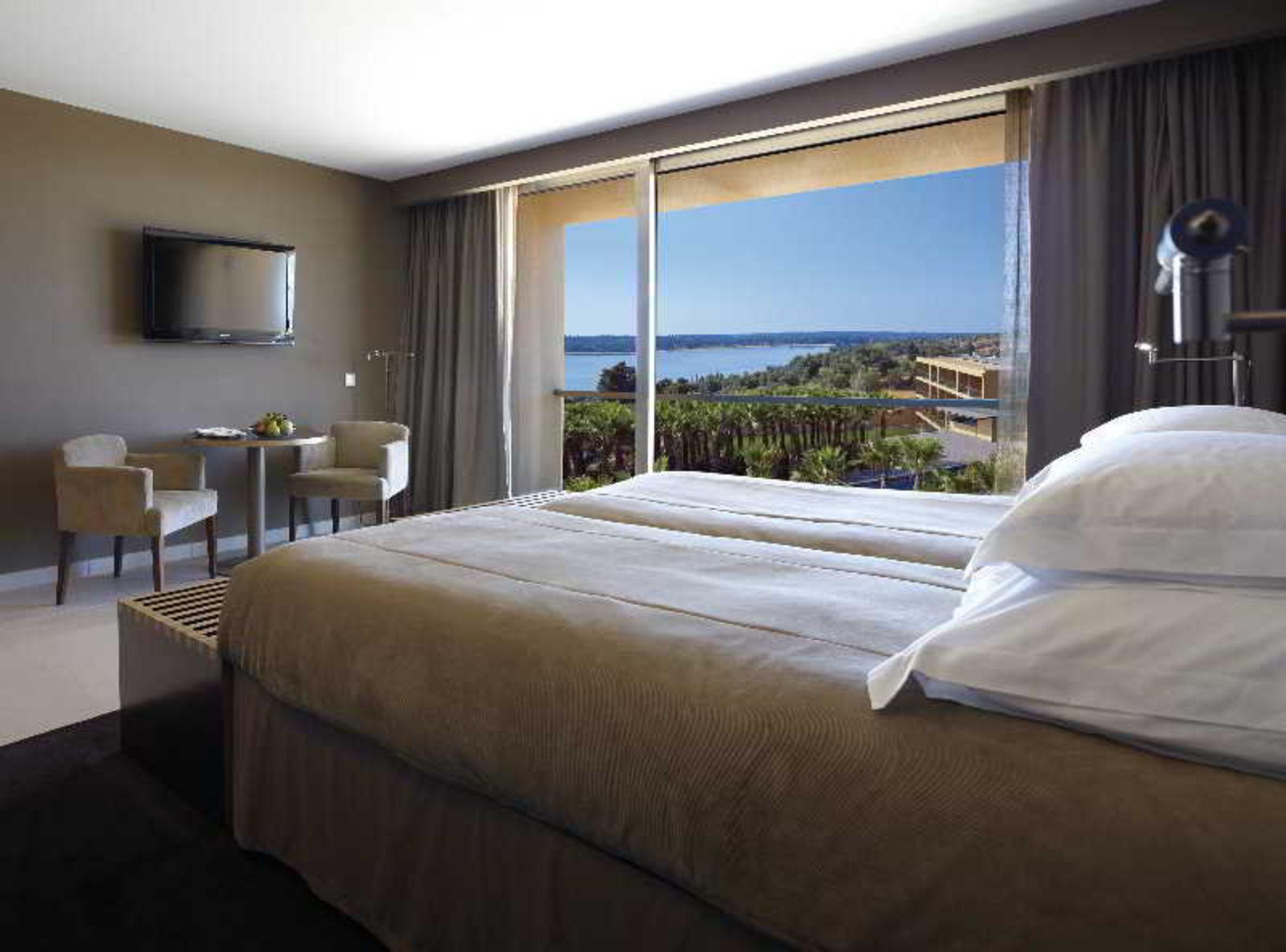 拉戈芒塔格别墅瑙酒店 蒙塔吉尔 外观 照片 The photo shows a modern hotel room with a large window offering a view of the sea and mountains. The room features a comfortable bed with white pillows and brown bedding. There is a small sitting area with two chairs and a table, as well as a wall-m
