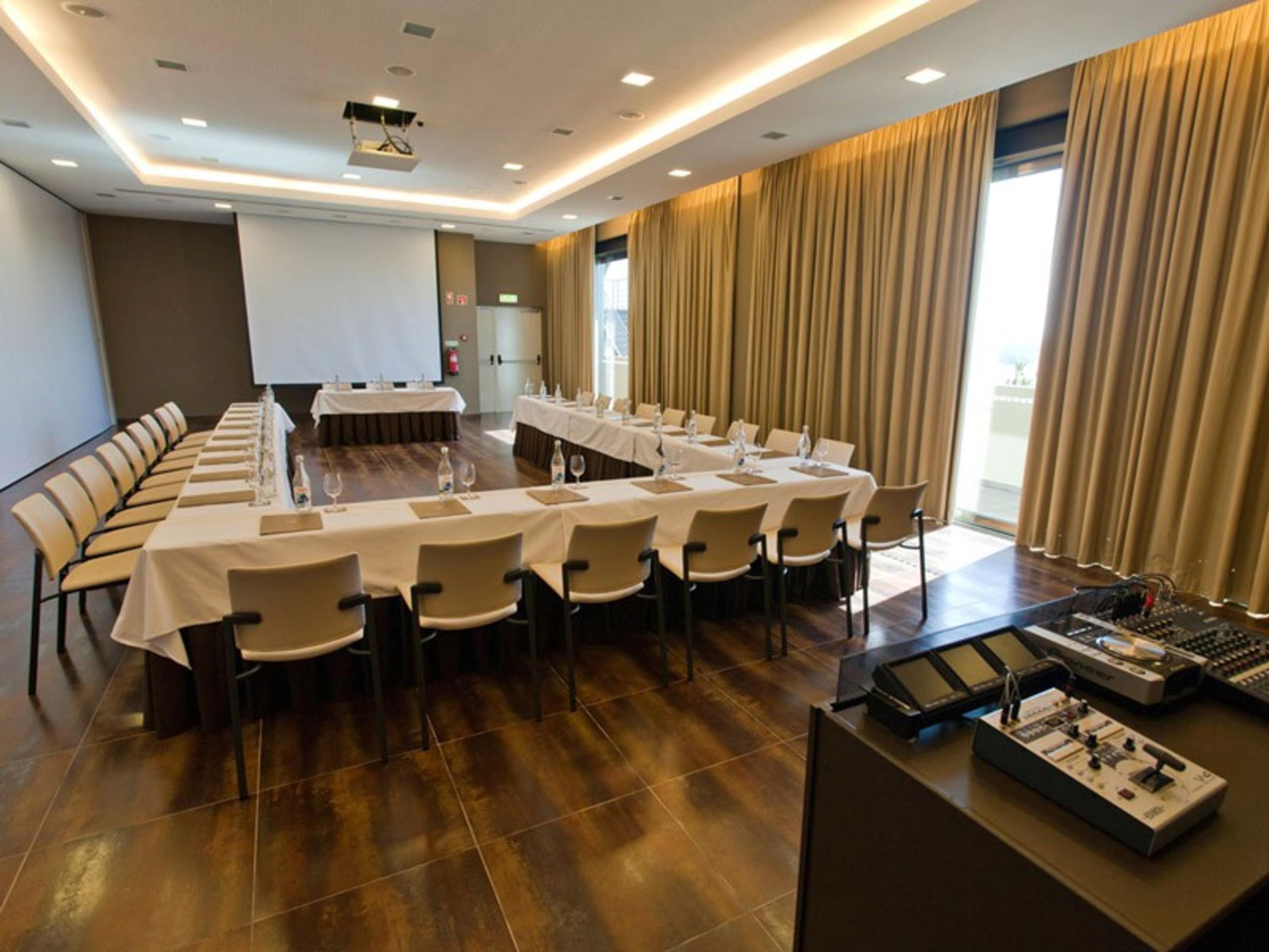 拉戈芒塔格别墅瑙酒店 蒙塔吉尔 外观 照片 The photo shows a modern conference room set up for a meeting. There are several tables arranged in a U-shape, surrounded by chairs. A large screen and projector are positioned at the front, with a table for speakers or presenters. The room has large